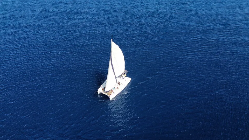 Voilier naviguant sur une mer bleu profond, vu du ciel